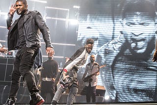 Usher dances on stage in all black in front of background dancers.