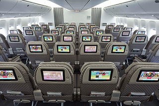 Rows of seats in an airplane with touch screens in front of each seat