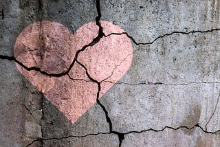 A heart painted on a cracked concrete wall. The crack runs through the heart, dividing it into three pieces.