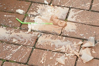 Splattered milkshake and broken glass on a brick pavement ground.