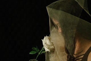 woman draped in white gauze holding a white rose — photo by Frances Beatty