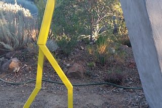 A yellow stick figure holding up a wall leaning into it made of metal artist unknown gallery in Walnut Creek CA 2017