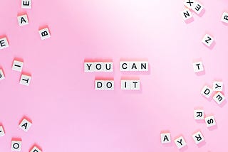 A pink background with white letter beads scattered around the sides. In the middle, in the same letter beads, it says “You Can Do It”