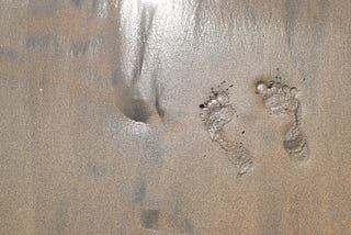 Sand mixed with mud and two footprints washing away.