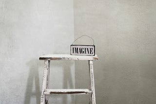 A white painted ladder has a sign on it that reads, “IMAGINE.”