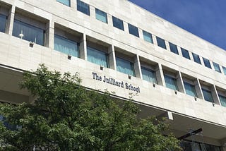 Picture of the exterior of The Juilliard School, with white stone exterior and a blue sky in the background