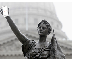 Bronze statue (“Forward”) of woman with arm raised. Smartphone is photoshopped in her hand, screen has BenchK12 company logo.