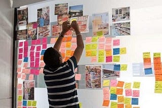 Young man plotting out a service by assembling post it notes and images on a light board to bring a service to life.