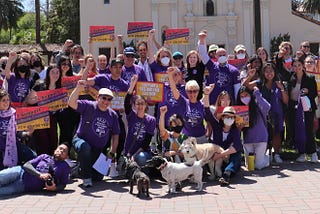 A group of people in purple shirts with fists up in the air on a college campus