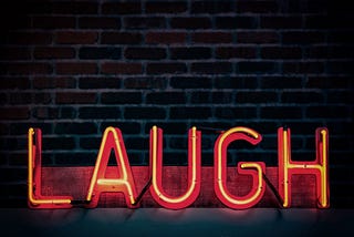 A red neon sign reading “LAUGH” against a dark brick background