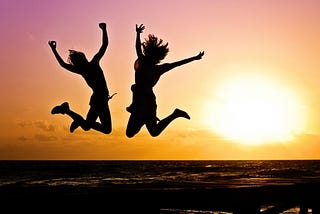 Two people jumping into the air in front of the sunset and the ocean