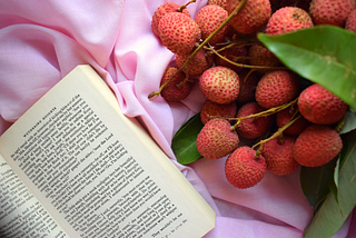 An open book on a pink sheet, besides a bunch of strawberries