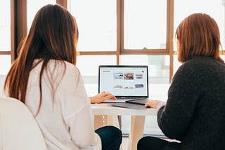 Two women work while sharing a laptop on the table.