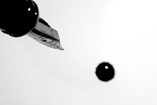 A fountain pen dripping a blob of ink onto a white paper