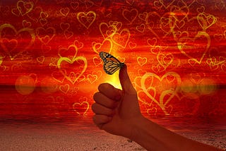 Against a backgroud red with yellow hearts, a butterfly perches on a person’s thumb.