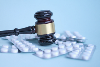 A judge’s gavel surrounded by medication tablets.