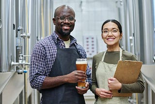 two employees holding a glass of beer smiling.