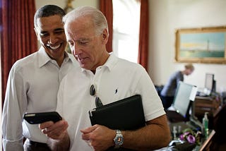 Joe Biden and Barack Obama look together at a cell phone