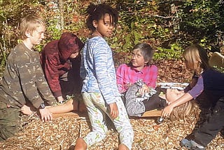 children gather around in a mock funeral as one child pretends to be dead