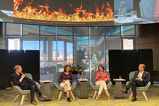 Four speakers in chairs discuss hope and despair in global futures. The screen above them shows a fire.