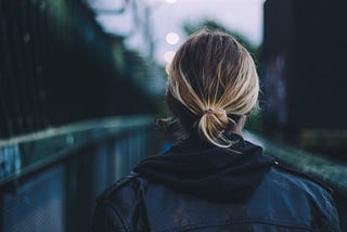 Photo of a person in a leather jacket crossing a bridge taken from behind