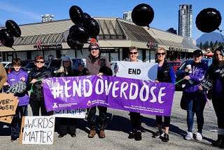 Members of the Tri-Cities Community Action Team are holding black balloons and a big purple sign with the words #End Overdose.