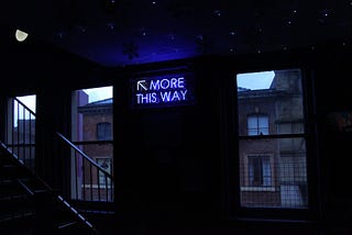 staircase with a neon sign next to it that says “More this way”