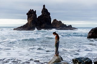 Lonely woman standing on a rocky coast surrounded by ocean