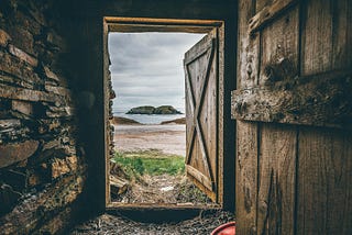 View looking out from the inside of a dark rustic shed onto a quiet beach