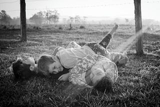 three boys wrestling on the grass late in the day