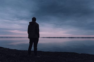 Silhouette of a man standing by a lake in the dark