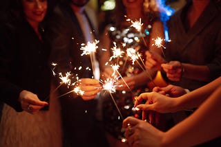 A group of friends’ hands hold out sparklers to welcome the new year.