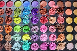 A close up of an eyeshadow palette featuring a rainbow of colors, some of which are broken