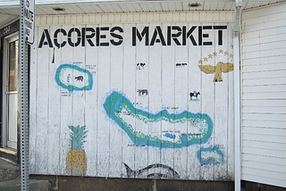 A map of several islands of the Azores painted on the side of a small building. Decorating the map are the golden goshawk and stars of the Azorean flag, a whale, a pineapple and some cows.