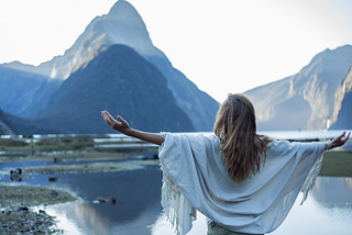 Woman with her arms open facing a beautiful mountain peak