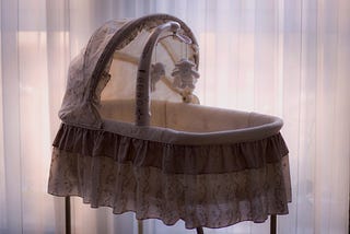An empty baby bassinet in muted colors with moody lighting