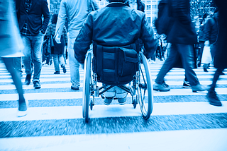 A person in a wheelchair using a crosswalk on a busy city street.