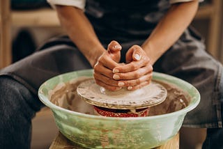 Person sitting at potters wheel beginning work on a ceramic masterpiece.