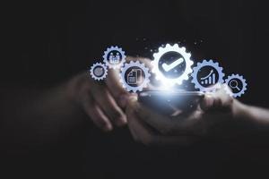 In the image, a pair of hands holds a smartphone from which a cascade of gear-shaped icons emerges, symbolizing different facets of digital services like analytics, user profiles, and settings, illustrating the concept of technology at one’s fingertips.