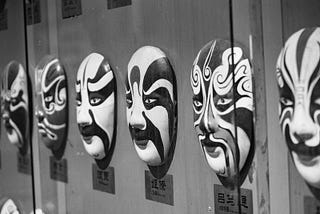 A row of kabuki masks hung on a wall, shot from an angle. ( in black and white)