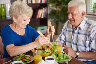 Older woman and man smile while eating a salad.