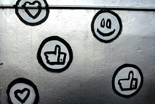 Social media icons including a smiley face, hearts, and thumbs up are painted in black and white on a metal surface.