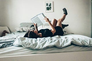 A girl reading on bed, with her feet in the air.