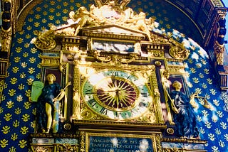 A photo of an ornate golden clock with statues on either side, golden ornamentation, and many different symbols.