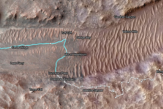 This Mars Reconnaissance Orbiter image shows a dune filled dry river bed cutting across the otherwise rocky Mars landscape. Superimposed on an image from NASA’s Mars Odyssey orbiter, this map shows Perseverance’s path between Jan. 21 and June 11. White dots indicate where the rover stopped after completing a traverse beside Neretva Vallis river channel. The pale blue line indicates the rover’s route inside the channel. Credit: NASA/JPL-Caltech/University of Arizona