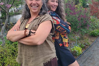 two women smiling arms crossed standing back to back