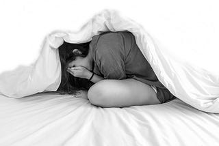 Woman under a blanket with her face in her hands