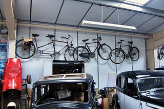 Old bicycles mounted on the wall above cars in a motor museum.