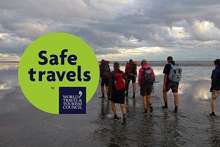 Safe Travels logo with group of tourists hiking along a beach