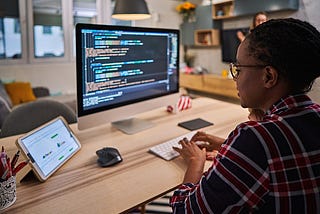 Woman sitting at a desk writing lines of code on a computer.